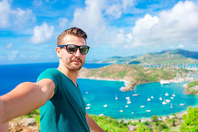 在加勒比海热带岛屿安提瓜岛的天堂湾，一名年轻人在雪莉高地(Shirley Heights)上自拍英国港的景色